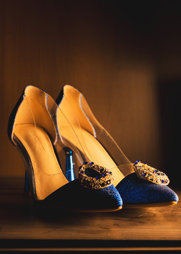 A pair of elegant blue stiletto heels with embellished buckles in warm ambient light.