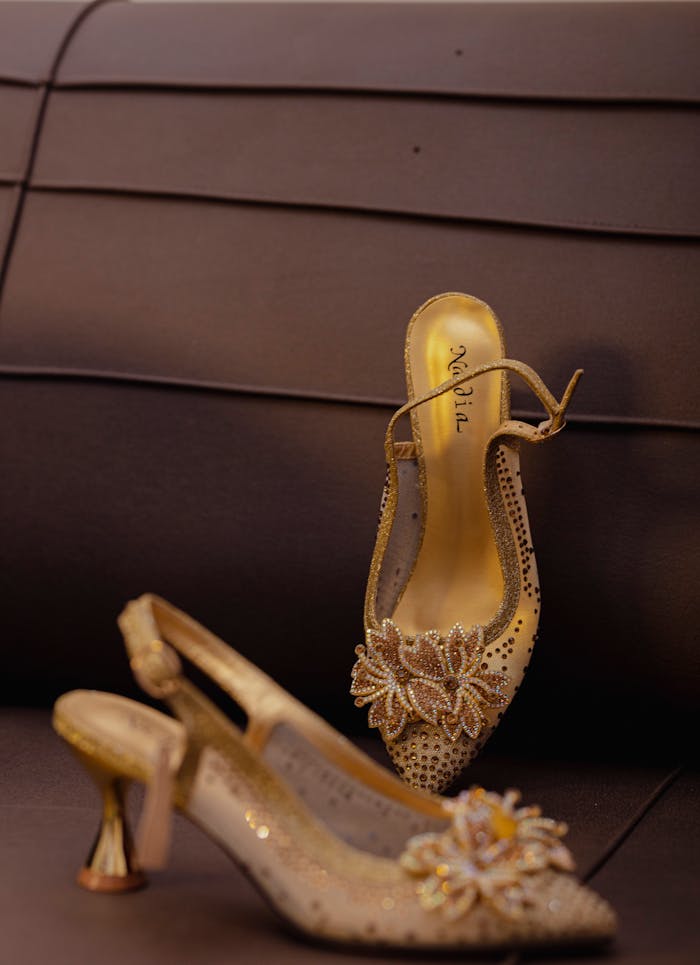 Elegant gold stiletto heels with floral adornments displayed against a chic brown backdrop.